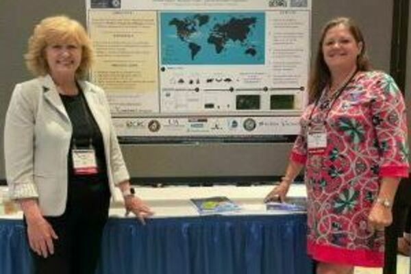 2 women stand in front of a scientific poster.