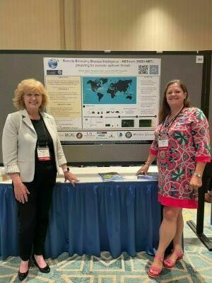 2 women stand in front of a scientific poster.